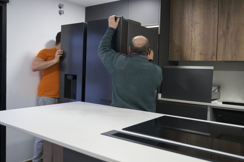 Two technicians installing an american fridge in a new modern kitchen.